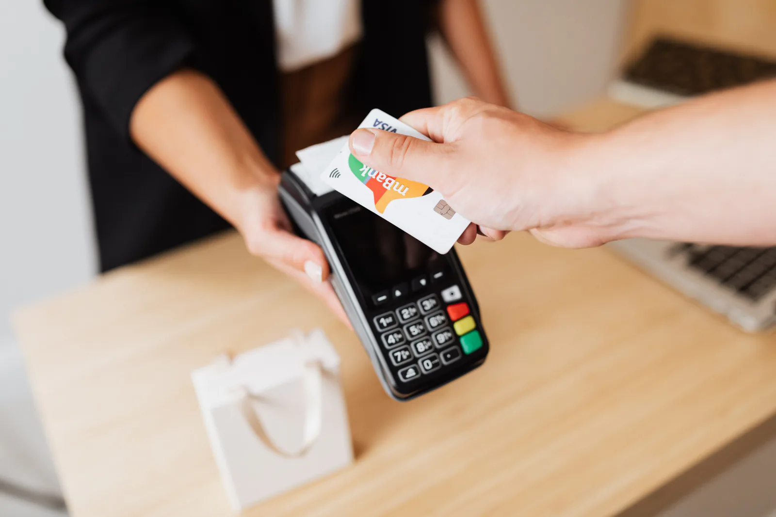 Hand tapping a contactless card on a payment terminal at checkout, declining dynamic currency conversion abroad