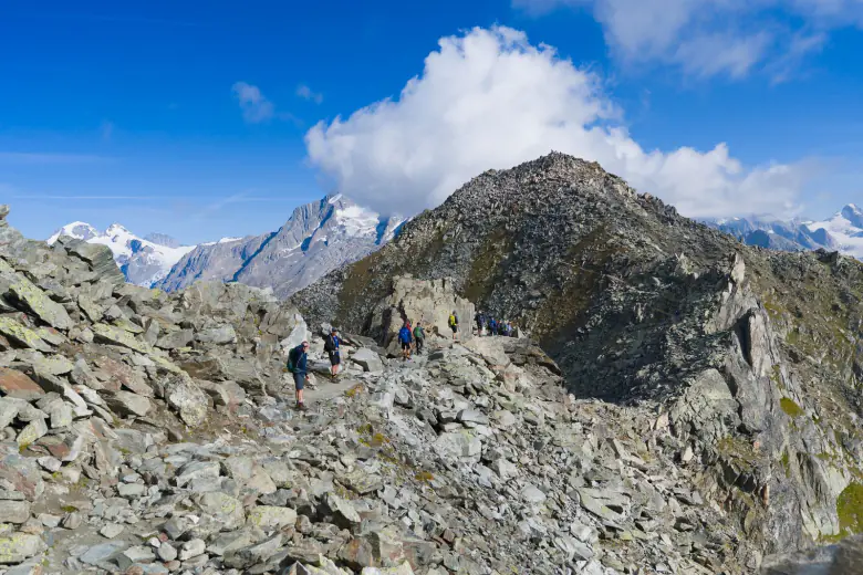 Hikers crossing a rocky ridge with glaciated peaks behind – classic 11-stage TMB itinerary, Alps