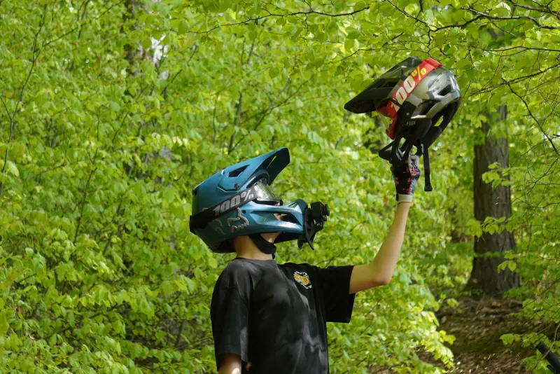 Rider in a full-face helmet holding a second helmet in the forest – gear and insurance for Whistler, BC
