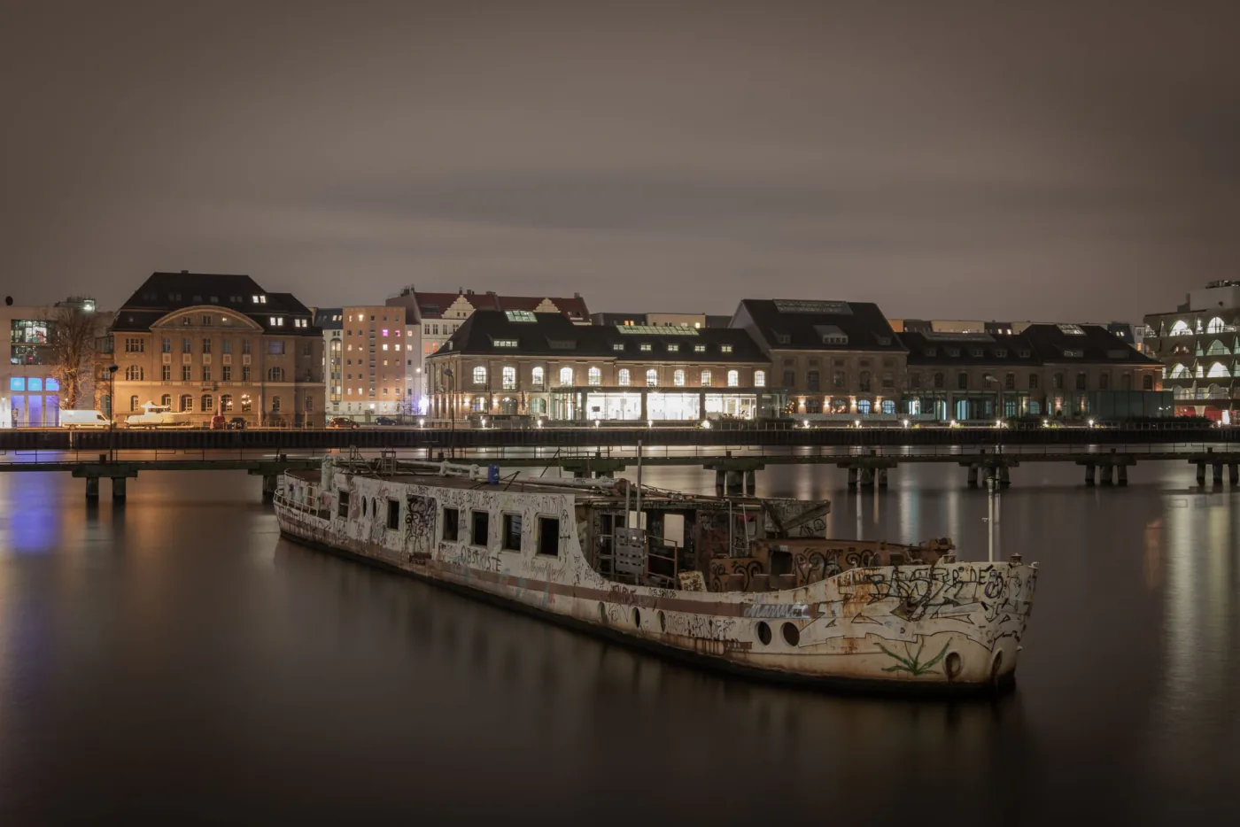 Urban nightscape in Berlin showcasing an illuminated waterfront with an abandoned shipwreck on the Spree River. – Where should you go sober clubbing in Berlin?