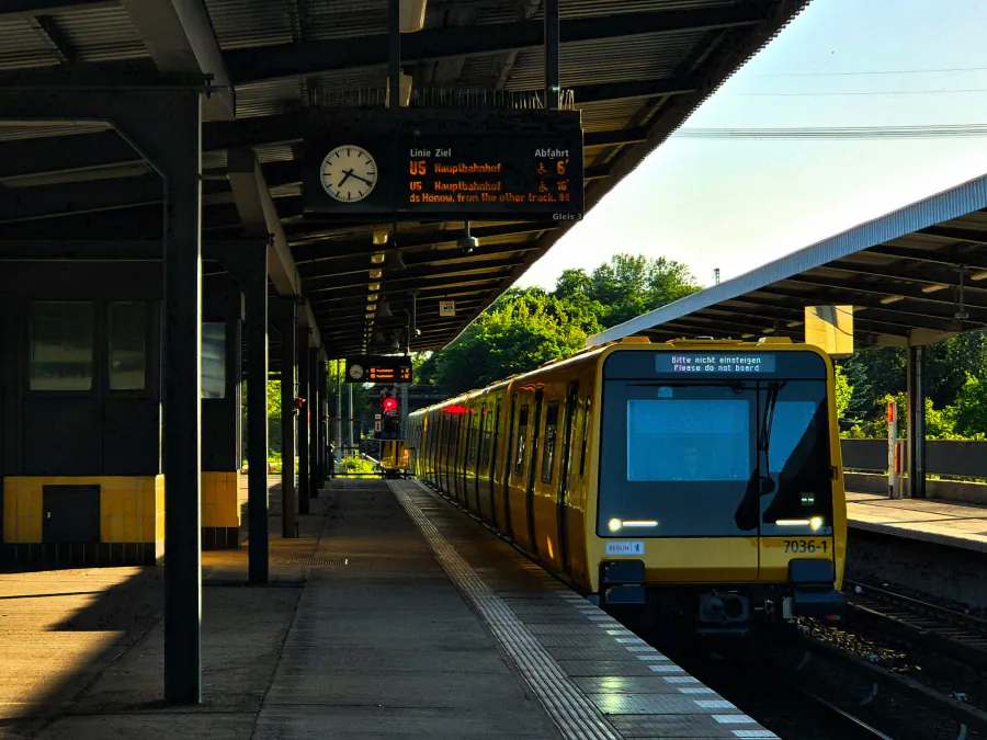 A yellow metro train arrives at a Berlin outdoor station during sunrise, showcasing modern urban transport. – How do you get to Berlin — and home from the club 