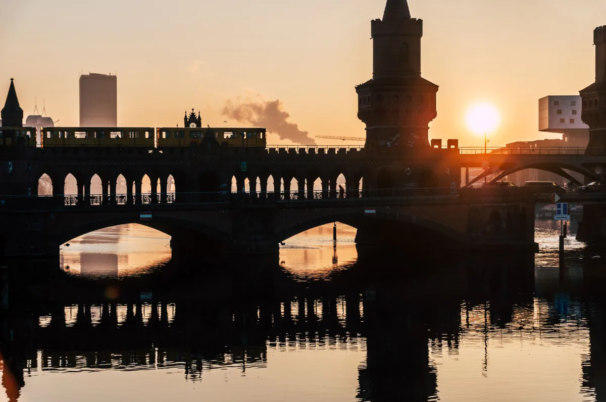 A cityscape featuring Berlin's iconic Oberbaum Bridge at sunrise, with a train crossing above. – How do you last ten hours on the floor without alcohol?
