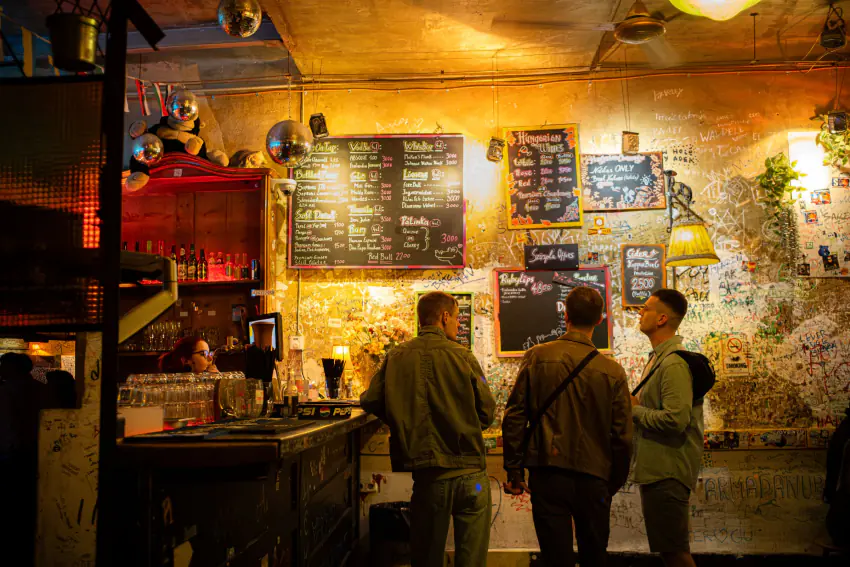 Friends comparing drinks inside a Budapest ruin pub under eclectic lighting – Belgrade vs Budapest: which city should you party in?