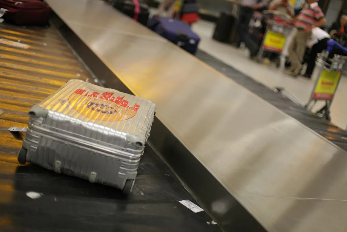 Grey hardshell suitcase waiting on an airport baggage belt - the real cost of adding a checked bag