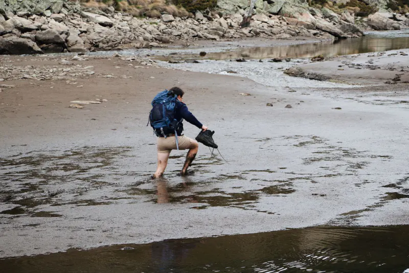 Hiker wading a cold glacial river holding boots – Laugavegur gear and river crossings, Iceland