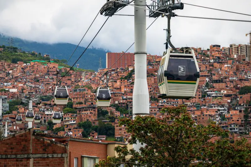 Cable cars traversing the vibrant hillsides of Medellín, with terracotta buildings and lush greenery below. – How Do You Get Around Medellín at Night — and In f