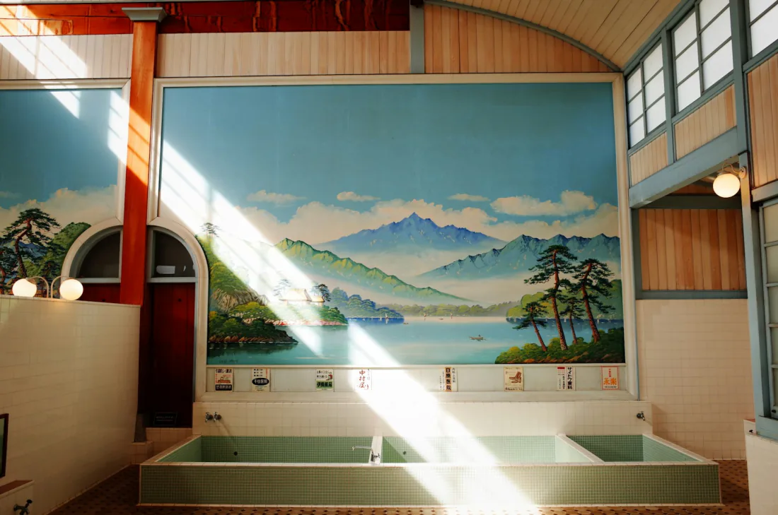 Tiled sento bathing hall with a painted mountain mural and taps above the tubs – pre-bath washing ritual section, Japan