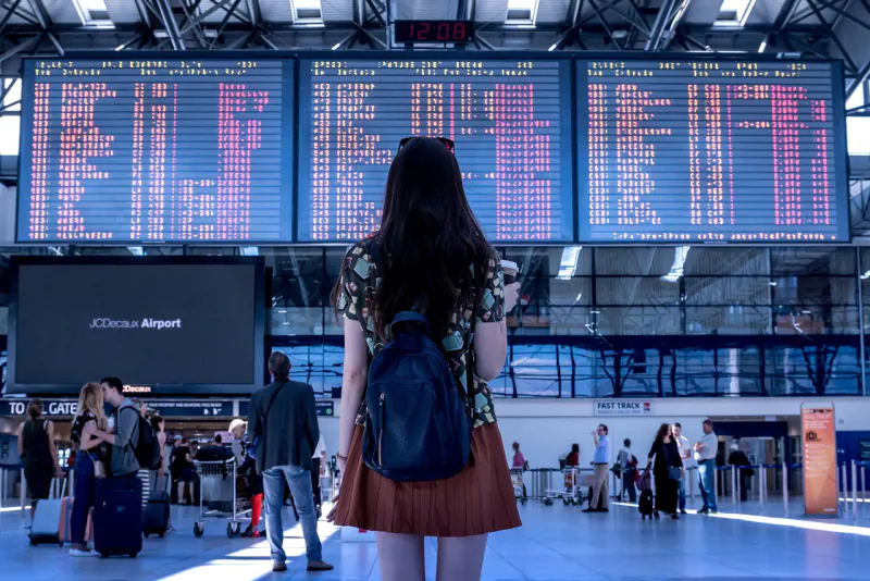 Woman with a backpack reading a large split-flap departures board – what happens when you miss the second leg