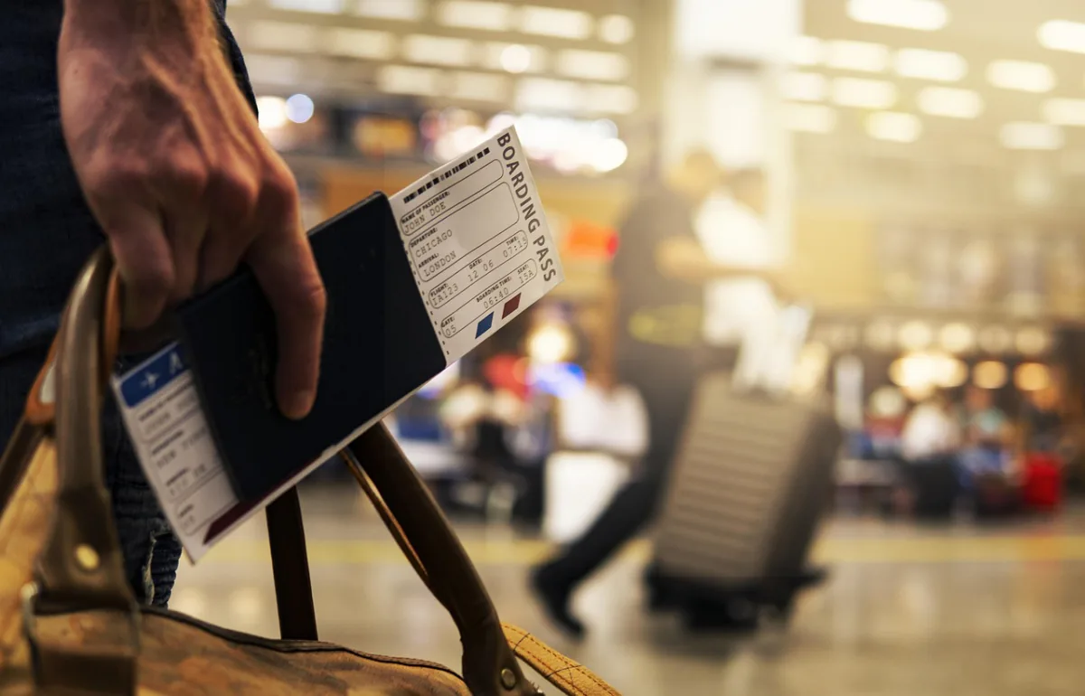 Hand holding a passport and boarding pass beside a leather travel bag – protecting a two-ticket itinerary