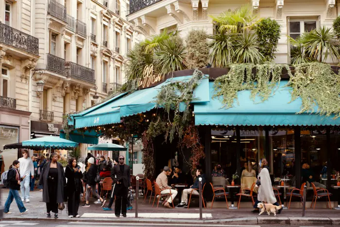 Parisian cafe terrace with turquoise awning and diners on a busy street – arriving in Paris on an open-jaw flight