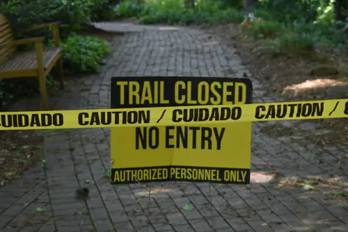 Trail closed sign with caution tape blocking pathway in a park setting. – What Do Festival Insurance Policies Exclude?